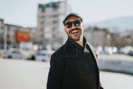 Lächelnder stilvoller Mann mit Sonnenbrille genießt sonnigen Wintertag in urbaner Umgebung.