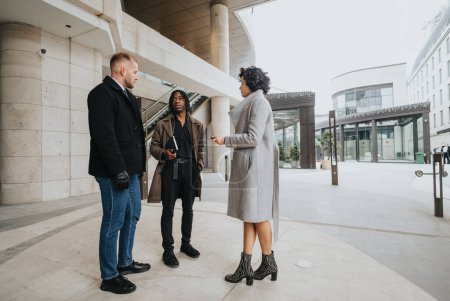 A group of three diverse business people conversing outside a contemporary building, with an air of collaboration and teamwork.