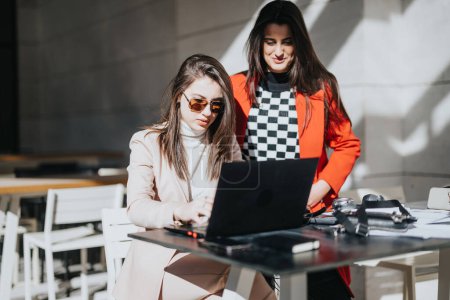 Zwei stilvolle Geschäftsfrauen kollaborieren bei Laptop im Outdoor-Café.