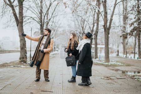 A trio of young business colleagues in winter attire navigate a snowy city park, displaying teamwork and adaptation to cold weather conditions.