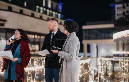 Ein engagiertes Team von Kreativen, die an einem Winterabend im Freien arbeiten, beleuchtet von warmen, festlichen Lichtern in urbaner Umgebung.