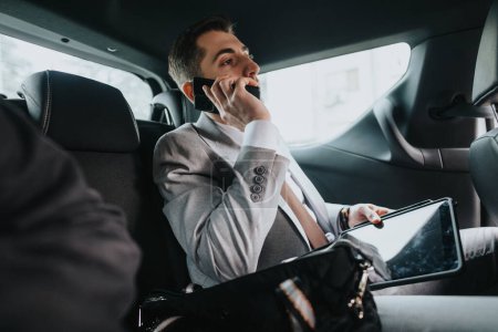 Homme d'affaires professionnel en costume utilisant un téléphone intelligent et une tablette tout en voyageant en voiture, mettant en valeur le mode de vie d'affaires moderne.