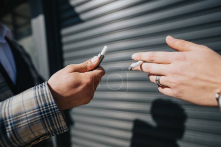 Deux professionnels se tiennent dehors dans un cadre urbain, partageant un moment autour d'une cigarette pendant une pause de travail.