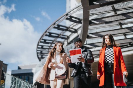 Les jeunes collègues d'affaires dans des tenues élégantes marchent ensemble à l'extérieur, engagés dans la discussion avec une tablette numérique dans la main sous l'architecture moderne.