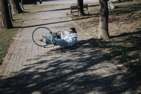 Ein Radfahrer ist in einem sonnenbeschienenen Park von seinem Fahrrad auf einen Ziegelweg gestürzt und hat einen Moment eines unerwarteten Unfalls festgehalten.