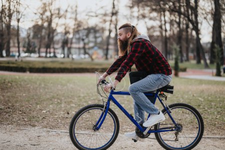 Hipster man with beard rides a bicycle through a peaceful park setting as evening approaches, conveying a sense of leisure and freedom.