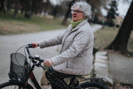 Mature female retiree taking a leisurely cycle through tranquil park scenery.