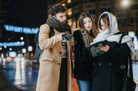Group of young adults engaging in a collaborative effort, using a tablet on a bustling city street illuminated by night lights.