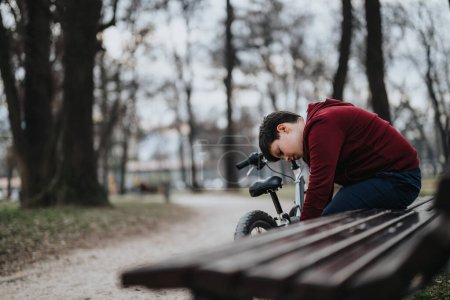 Un momento reflexivo capturado mientras un niño descansa en un banco junto a su bicicleta, rodeado de la serenidad de la naturaleza.