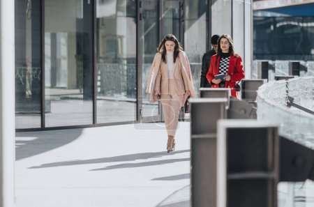 Dans cette image, deux femmes et un homme professionnels sont capturés marchant en toute confiance dans un environnement urbain, mettant en valeur des vêtements de travail modernes.