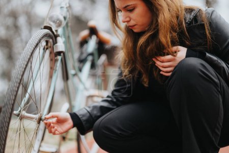 Stylish and confident young businesswoman in an elegant black outfit repairing an old bicycle on a cloudy day