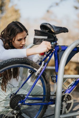 Eine konzentrierte junge Frau schließt ihr blaues Fahrrad an einem Ständer ab und sorgt so für Sicherheit im Park.