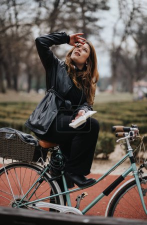 Elegante joven empresaria disfruta de un descanso de lectura al aire libre mientras se sienta en su bicicleta vintage en un parque escénico.