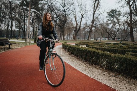 Confident and stylish young woman enjoys a peaceful bike ride through a serene park, embodying elegance and independence.