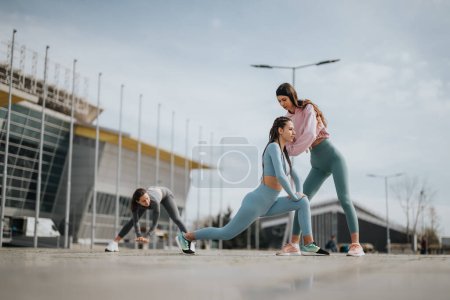 Fitness enthusiasts stretch on the pavement, preparing for exercise with urban architecture in the background.