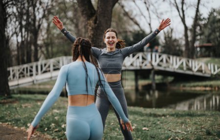 Zwei athletische Frauen in Sportkleidung feiern fröhlich ihre Outdoor-Trainingserfolge in einer landschaftlich reizvollen Parklandschaft.