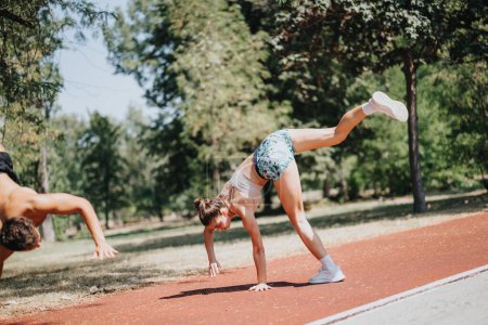Fit sportspeople, a man and woman in sportswear, doing cartwheels. They inspire with their athleticism and outdoor workout in a sunny park. Training and positive results lead to better body shape.
