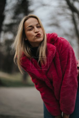 Stylish young woman wearing a vibrant pink faux fur coat in a natural setting during winter.
