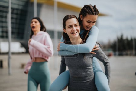 Two cheerful women embracing in workout attire, celebrating success with a joyful friend in the background