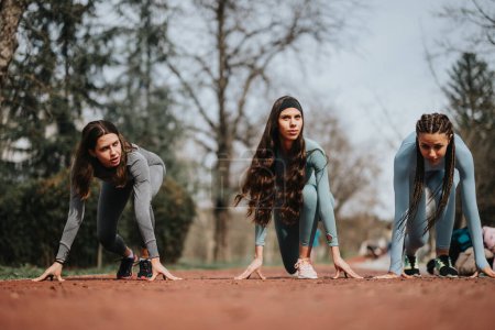 Athletic individuals bent over in ready position on a track, poised for a sprint in an outdoor setting