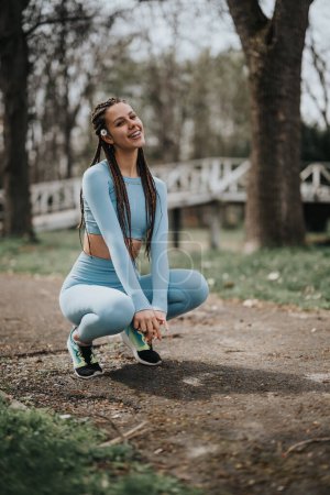 Active sports girl in workout gear outdoors, taking a break during a fitness routine in nature.