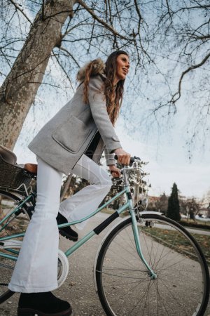 Mujer de negocios con un abrigo elegante montando una bicicleta vintage en un sendero del parque, encarnando los desplazamientos ecológicos.