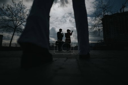Un couple se dresse silhouette contre un ciel lunatique, représentant la romance urbaine au milieu d'un paysage urbain dramatique.