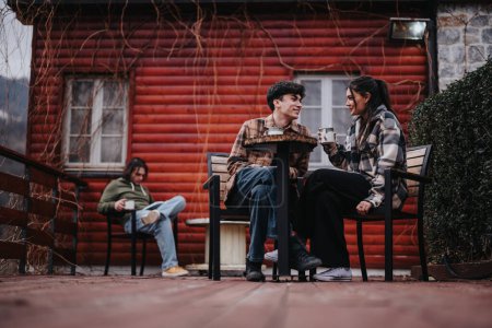 Junges Paar teilt einen Moment mit heißen Getränken auf einer rustikalen Hütten-Veranda und strahlt Wärme und Glück aus.