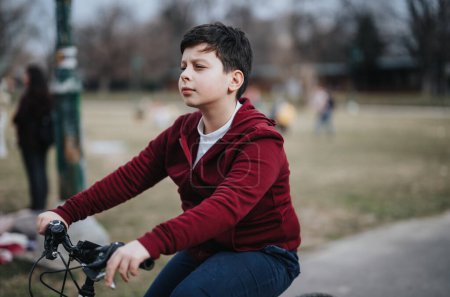 A young boy riding a bicycle, enjoying leisure time and fresh air in a city park surrounded by nature.