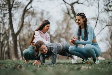 Three women engaging in a fitness routine outdoors, with one coaching the others in a serene park setting.