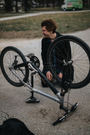 Young male entrepreneur showcasing problem-solving by fixing his bicycle in an urban park setting.