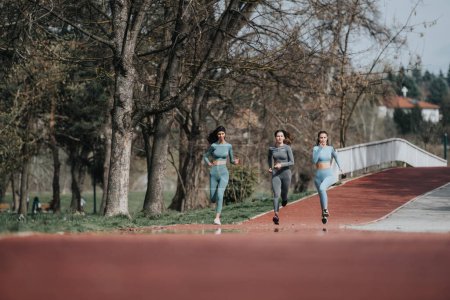 Mujeres activas corriendo juntas, disfrutando de un entrenamiento en un tranquilo parque con un puente y árboles en el fondo.
