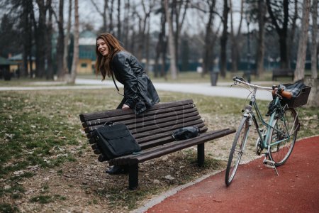 Stilvolle junge Geschäftsfrau mit Fahrrad macht auf einer Parkbank eine gemütliche Pause und strahlt Zuversicht und Glück aus.