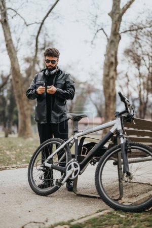 Modern male business entrepreneur in leather jacket using smart phone by electric bicycle in outdoor setting.