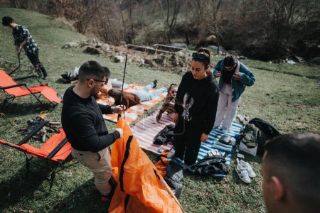 A group of young adults are seen organizing their camping gear in a natural, grassy setting. They are engaging in outdoor activities and appear to be preparing for a stay in the wilderness.