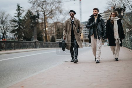 A group of three multiethnic business colleagues casually walking and talking along a city street, exuding teamwork and cooperation.