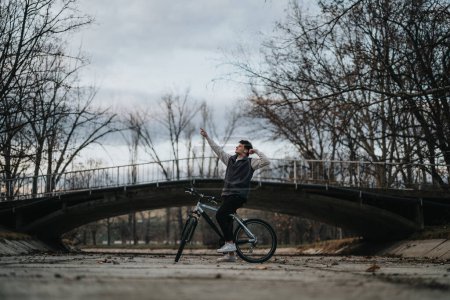 Teenage boy taking a break during a bike ride in a scenic park with a bridge in the background.