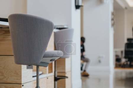 Vista centrada en una silla de oficina gris en un espacio de trabajo moderno con un fondo borroso de una persona que trabaja en su escritorio.