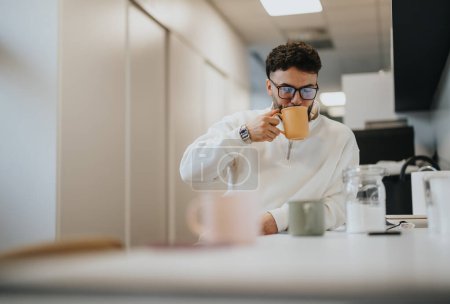 Handsome man taking a break from work. He is taking a sip of his tea while sitting at relaxing at the kitchen. Copy space.