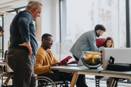 An inclusive modern office environment with a diverse team collaborating. A person in a wheelchair actively engages with colleagues.