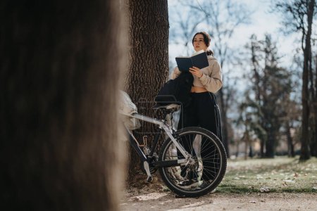 Ein junges Mädchen steht auf ihrem Fahrrad im Park, vertieft in die Lektüre eines Buches, verkörpert Entspannung und Wochenendstimmung.