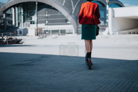 Professionelle Frau in stilvoller Businesskleidung mit einem Elektroroller als nachhaltigem Transport in einer städtischen Umgebung.