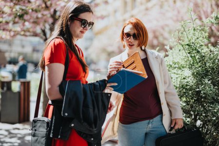 Two professional businesswomen in smart attire having a conversation while walking in an urban setting.