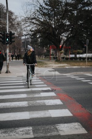A woman on a bicycle crosses a zebra pedestrian lane while the traffic light for pedestrians is green. An urban setting conveying commuting and eco-friendly transportation.