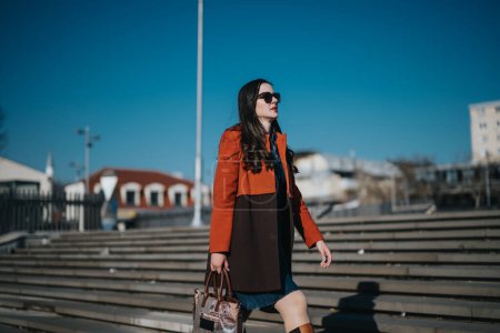 Mujer profesional con abrigo elegante que lleva un bolso mientras camina en un entorno urbano, que representa el equilibrio entre trabajo y vida.