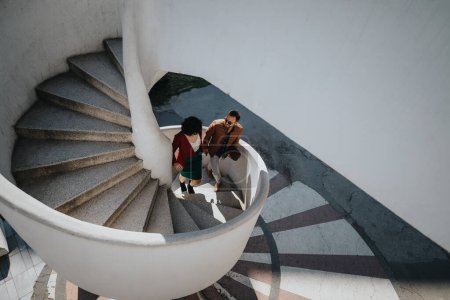 Two business colleagues in casual attire walking down a spiral staircase while having a discussion outside a building.