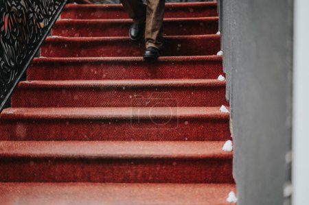 Plan détaillé des individus pieds montant les escaliers rouges saupoudrés de flocons de neige, dépeignant le mouvement lors d'une journée urbaine enneigée.