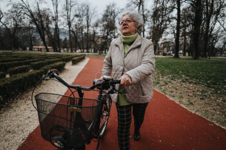 A mature female retiree with glasses stands with her bicycle in a park, showcasing an active lifestyle.