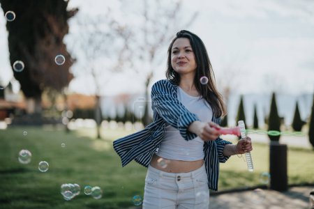 A cheerful young woman enjoying a sunny day outdoors by blowing bubbles in a park, showcasing a relaxed and joyful demeanor.