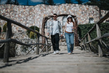 A cheerful young couple walks hand in hand across a charming wooden bridge, embodying the spirit of vacation and exploring new places together.